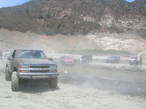 1985 Ford Bronco - Multiple vehicles navigate a dusty, off-road terrain with a mountainous backdrop.
