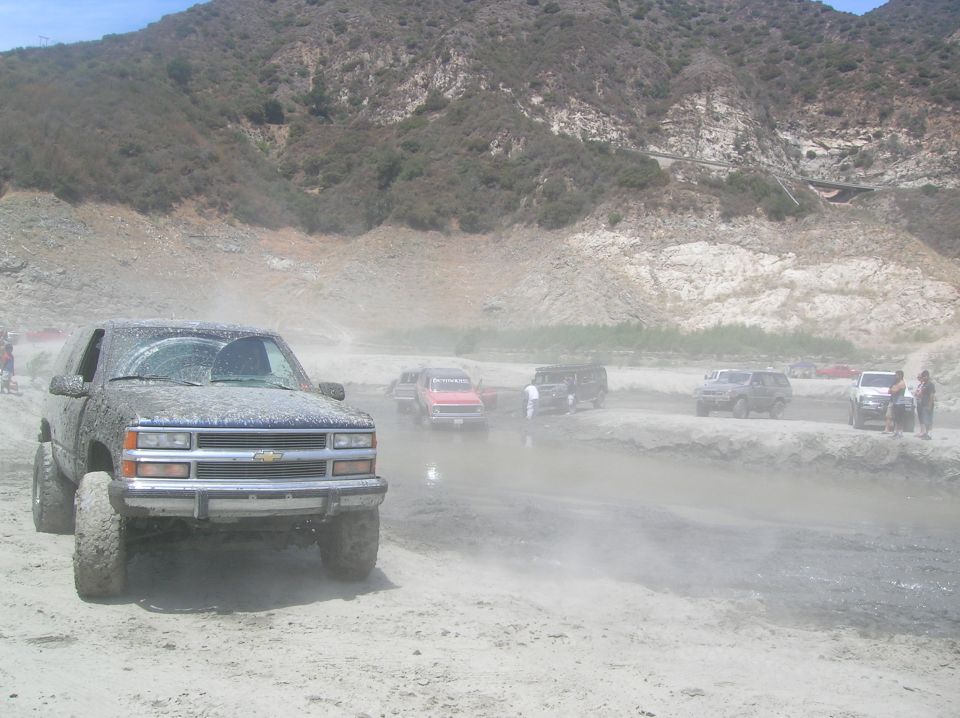 Several off-road vehicles are covered in mud and dust, with a mountain in the background
