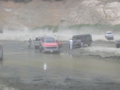 1985 Ford Bronco - Off-road vehicles navigate a muddy terrain, with some appearing to be stuck.