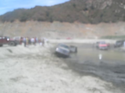 1985 Ford Bronco - Multiple off-road vehicles are stuck in a muddy area with a group of people observing.