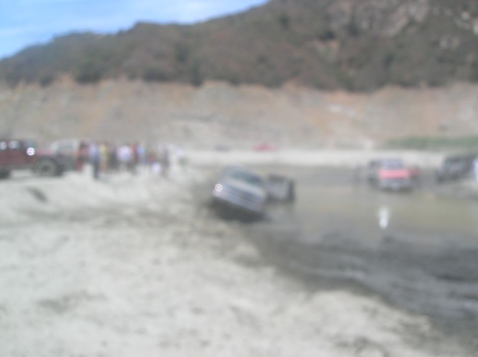 Several off-road vehicles are stuck in mud with people standing around