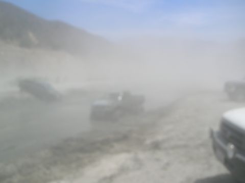 1985 Ford Bronco - Vehicles navigate a dusty off-road path, obscuring visibility and creating a hazy atmosphere.