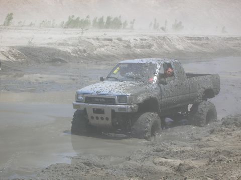 1985 Ford Bronco - Toyota pickup truck navigating a muddy off-road course, covered in mud.