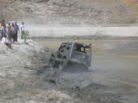 1985 Ford Bronco - An off-road vehicle is stuck in deep mud, with onlookers observing the difficult situation.