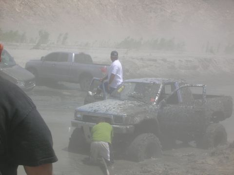 1985 Ford Bronco - Several off-road vehicles are stuck in thick mud, with people attempting to free them.