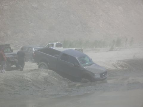 1985 Ford Bronco - Multiple trucks are stuck in the sand, indicating difficult off-road conditions.
