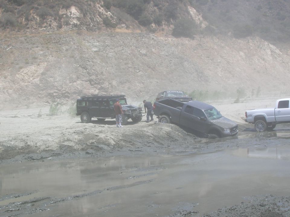 Several off-road vehicles are stuck in mud and sand near a rocky hillside