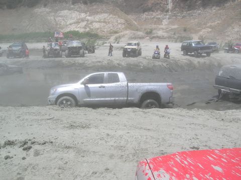 1985 Ford Bronco - Multiple off-road vehicles are stuck in the mud at a riverbed.