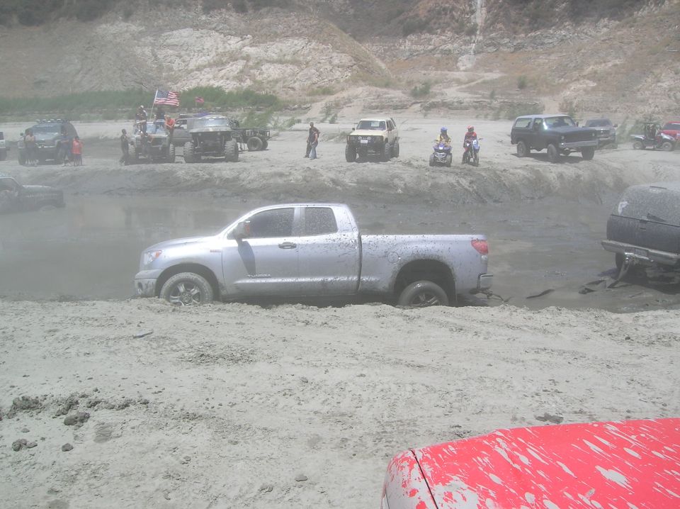 Silver pickup truck stuck in mud with other off-road vehicles in the background