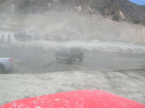 1985 Ford Bronco - Multiple vehicles navigate a dusty off-road trail with a hillside in the background.