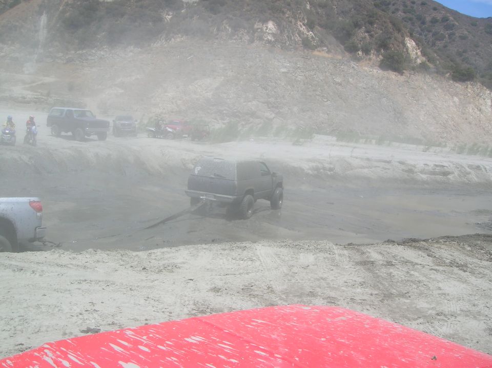 Several vehicles, including SUVs and ATVs, driving on a dirt track with dust clouds. A red object is in the foreground