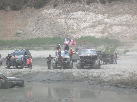 1985 Ford Bronco - Several modified off-road vehicles are gathered in a muddy, outdoor scene with people standing around them.
