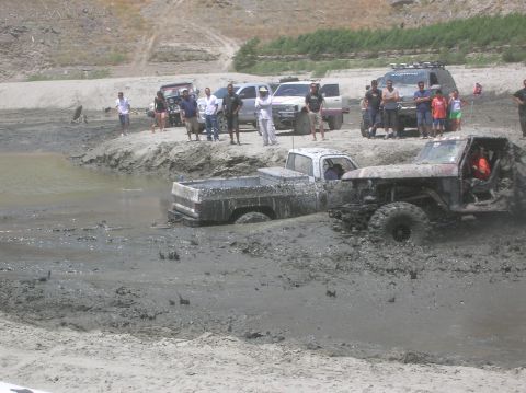 1985 Ford Bronco - Off-road vehicles stuck in mud during an event, with spectators observing.