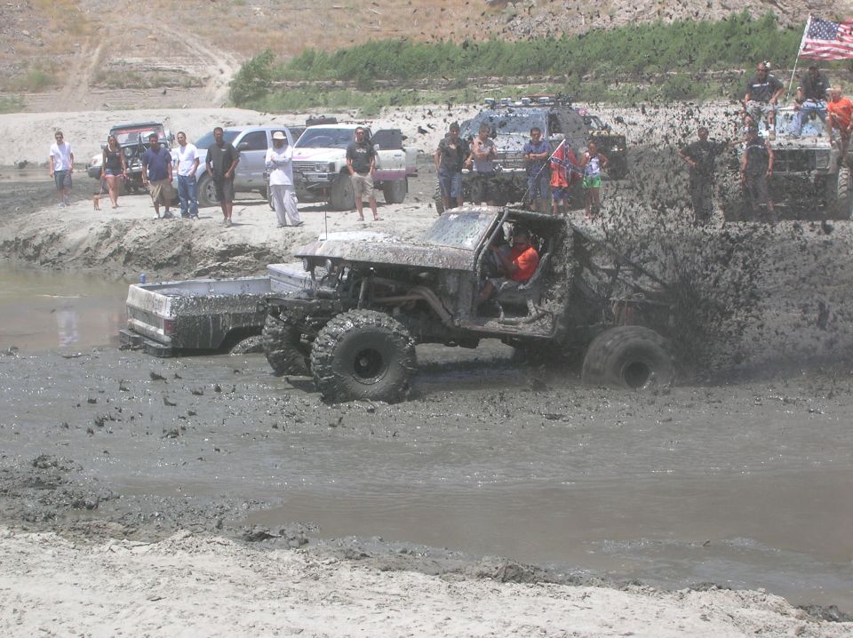 Muddy off-road truck splashing through a mud pit with people watching