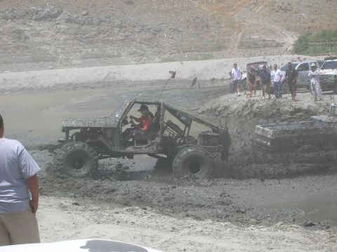 1985 Ford Bronco - An off-road vehicle churns through thick mud, with spectators watching from a dirt embankment.