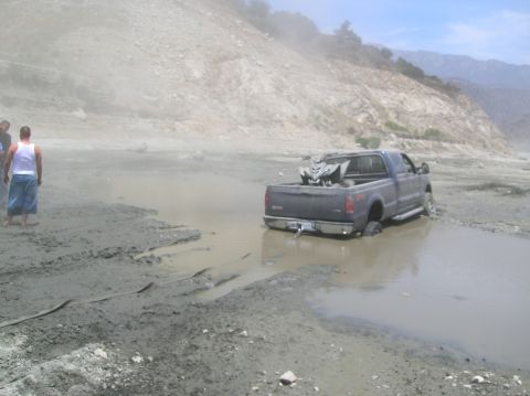 1985 Ford Bronco - A dark blue pickup truck is stuck in a muddy puddle with an ATV loaded in its bed.