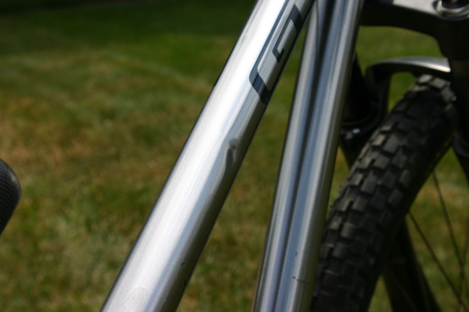 Close-up of a silver bicycle frame with a dent. Tire visible in background