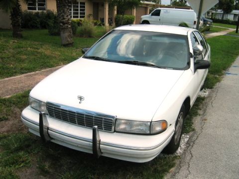 2001 Ford Crown Victoria - A white sedan is parked on the side of the road, with a white van visible in the background.