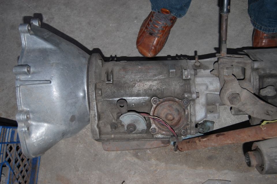 automatic transmission with wires and linkage visible, person's shoes in background