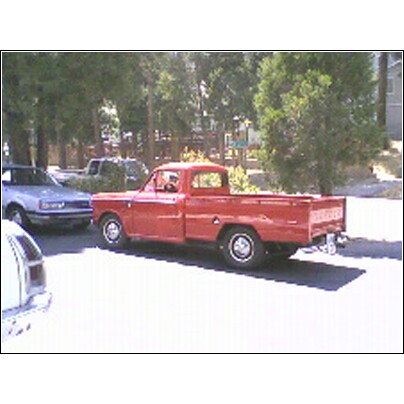 1973 Ford Ranchero - A red pickup truck is parked outdoors next to other vehicles under a canopy of trees.