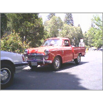 1973 Ford Ranchero - This red pickup truck appears to be from the 1950s, not a 1973 Ford Ranchero, and is parked next to another vehicle.