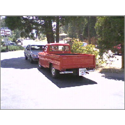 1973 Ford Ranchero - Rear view of a red pickup truck parked beside a silver sedan on a sunny day.