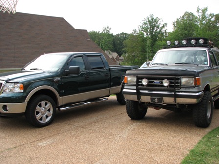 1991 Ford Bronco - Two Ford trucks are parked in a driveway. The Bronco has a light bar on its roof.