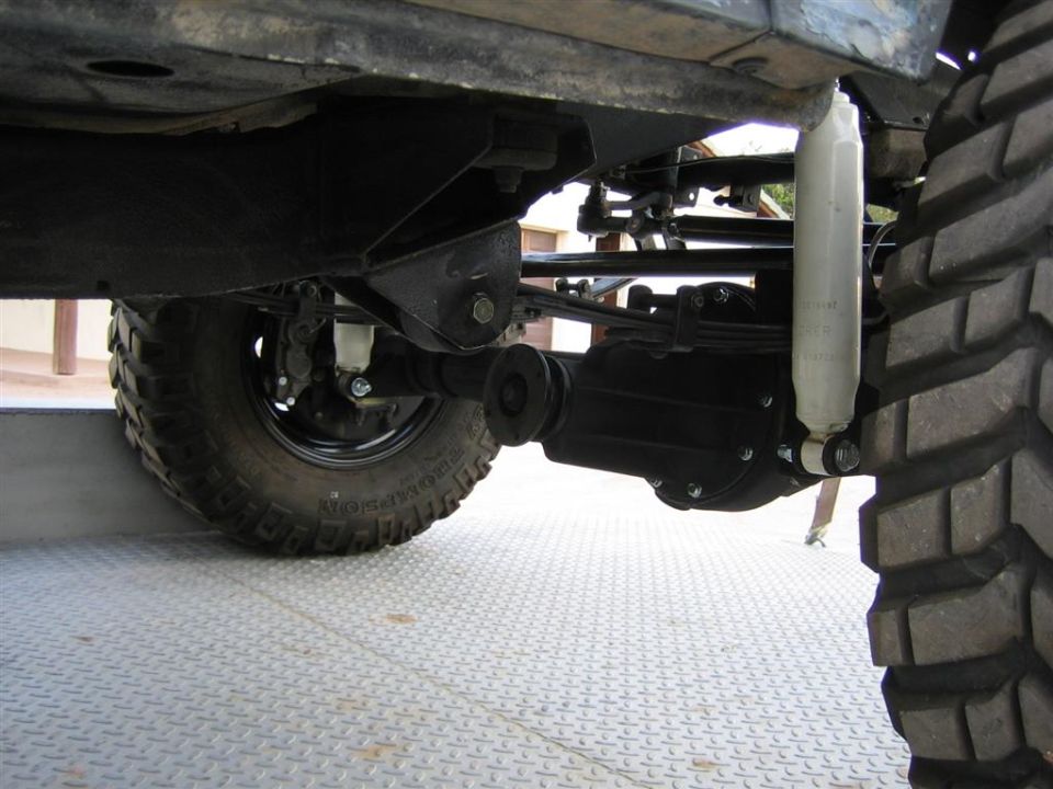 Underside view of black solid axle, leaf spring and white shock on a lifted 4x4