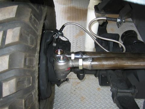 1987 Suzuki Samurai - Close-up view of a vehicle's steering linkage and a large tire, showing the tie rods and ball joints.