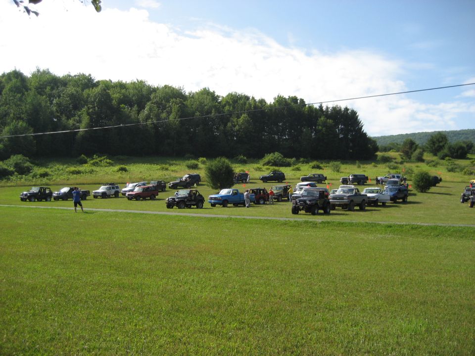 Group of off-road vehicles parked on a grassy field with trees in the background