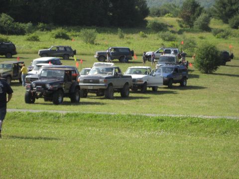 1991 Ford Bronco - A lineup of off-road vehicles are parked on a grassy field under a clear sky.