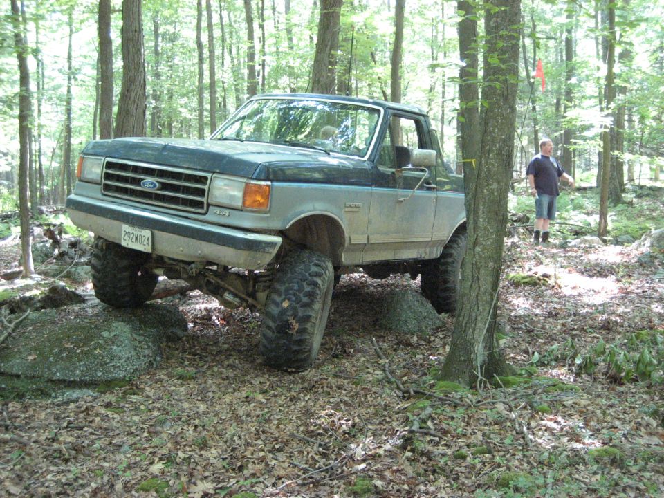 Ford F-Series truck on rocks in woods. License plate reads 292W024