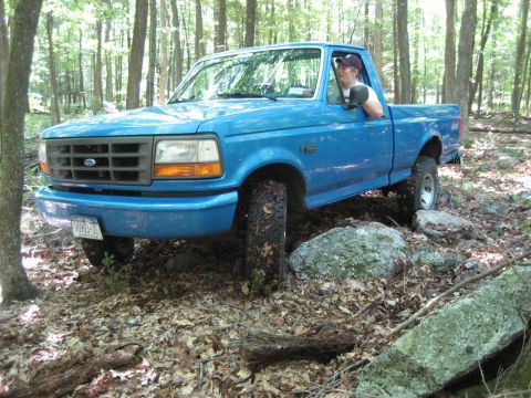 1991 Ford Bronco - A blue Ford F-150 navigates a rocky trail through a forest.