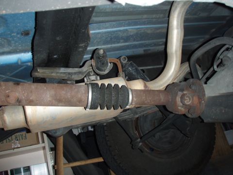 1996 Ford Bronco - The undercarriage of a vehicle shows the driveshaft, exhaust pipe, and suspension parts, with a rubber boot protecting a joint.