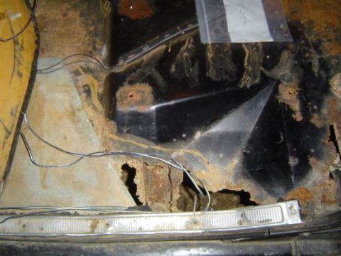1979 Ford Bronco - Stripped interior floor and rocker area of a truck cab showing severe rust-through with jagged holes in the floor pan and kick panel, loose…