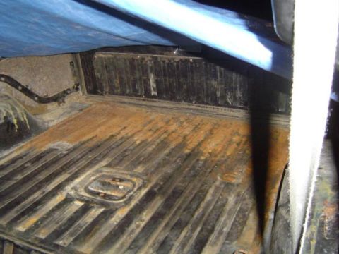 1979 Ford Bronco - The interior of a truck bed shows significant rust on its ribbed metal floor, partially covered by a blue tarp.