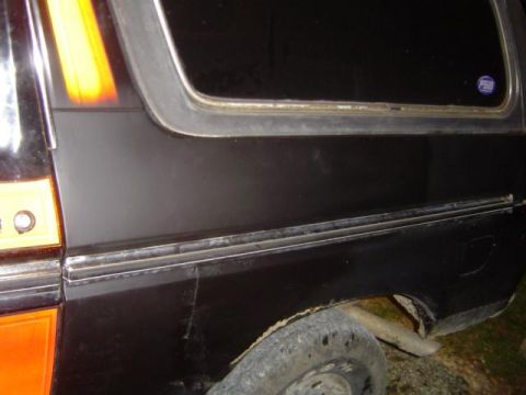 1979 Ford Bronco - The side of a black SUV shows a portion of its body with orange and yellow racing stripes and a chrome trim piece.