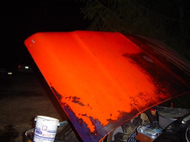 Orange vehicle hood with peeling paint, showing engine components underneath