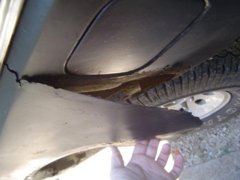 1979 Ford Bronco - The underside of a vehicle shows significant rust and damage to a metal panel near the wheel.