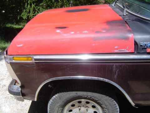1979 Ford Bronco - The front fender and hood of a maroon and red Ford Bronco show signs of age and wear.