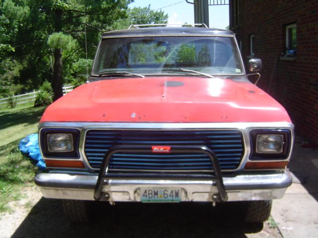 Front view of a red Ford Bronco with a black grille guard and a blue grille. License plate reads 4BM 64W