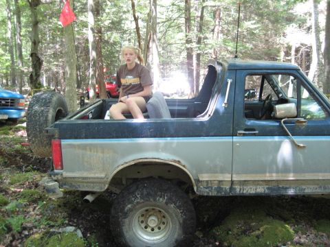1991 Ford Bronco - A young woman sits in the open rear of a Ford Bronco parked in a wooded area.
