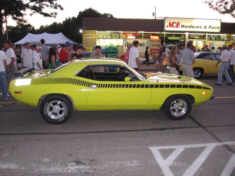 1989 Ford Mustang - A bright yellow Plymouth Barracuda is parked on the street in front of a store.