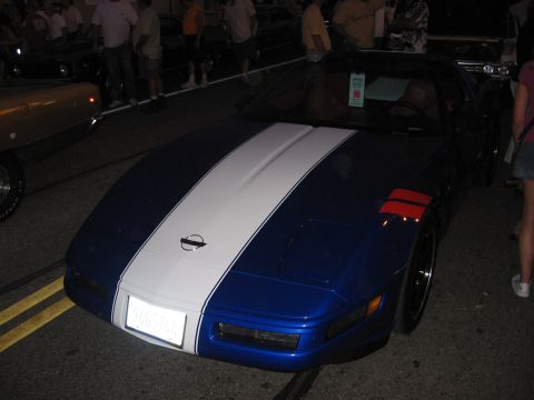 1989 Ford Mustang - A blue Chevrolet Corvette with white racing stripes is parked on a street at night.