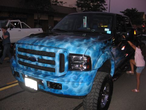 1989 Ford Mustang - Custom painted Ford F-Series truck with a blue flame design. A child climbs aboard while another vehicle waits nearby.