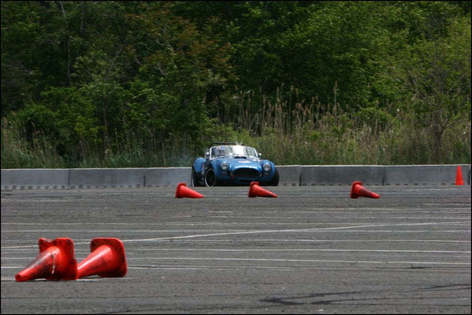 Blue convertible sports car with white racing stripes on a track, surrounded by orange cones