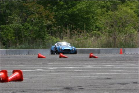 2001 Mercury Grand Marquis - A blue AC Cobra replica with white racing stripes is seen on an autocross course, maneuvering around orange cones.