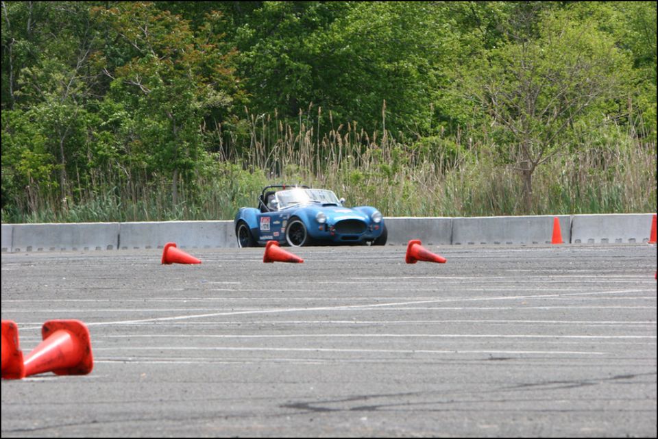 Blue convertible sports car with racing decals on a track, surrounded by orange cones