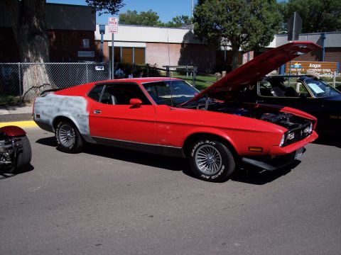 1972 Ford Ranchero - A red coupe with a primer-grey rear quarter panel sits with its hood open, parked next to another vehicle.