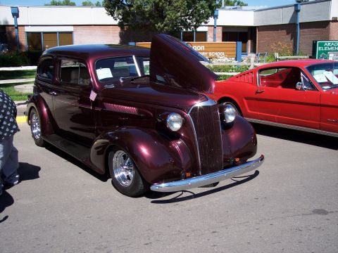 1972 Ford Ranchero - A classic maroon sedan hot rod is displayed with its hood up, parked beside a red sports car.